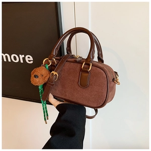 Détail du sac bandoulière en daim marron foncé avec breloque ours et fermetures dorées