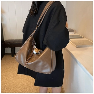 Detail of a brown Hobo tote bag showing soft matte leather and woven charm on a model