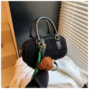 Détail du sac cylindre noir mat avec breloque ours et cordon vert sur tissu blanc