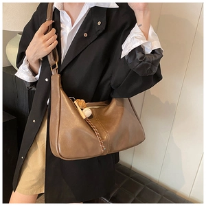 Detail of dark brown crescent bag with creative baseball charm and soft leather texture