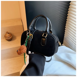 Détail du sac bandoulière vintage noir mat avec breloque chiot en peluche sur marche en pierre