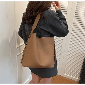 Detailed view of a brown pebbled leather tote bag worn by a model in a minimalist room