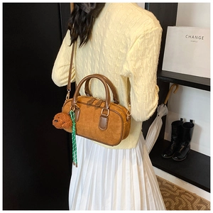 Détail d'un sac à main marron en daim mat avec breloque chien en peluche et métal doré