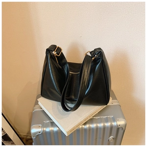 Detail view of the black leather shoulder bag with gold zipper on a silver suitcase
