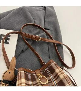 Detail van de verstelbare leren riem en geruite emmertas met konijntje hanger