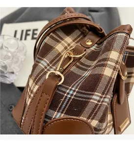 Detailopname van gouden metalen gesp en bruin geruite stof van de crossbody emmer tas