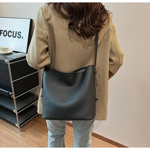 Black lychee leather bucket bag with adjustable strap worn as a crossbody bag