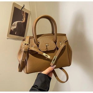 Detail of brown litchi leather handbag with gold metal hardware and turn-lock closure