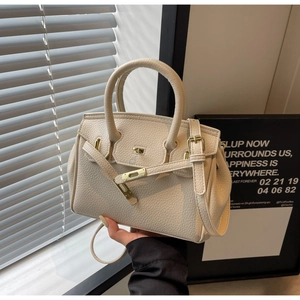 Detail shot of beige pebble grain leather surface and gold metal lock on the handbag