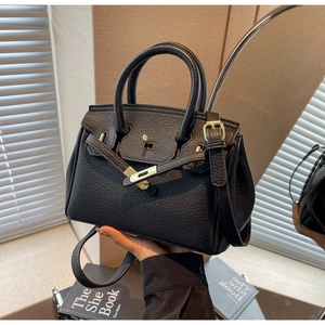 Detail of black lychee grain leather handbag with gold metal lock and classic top handle