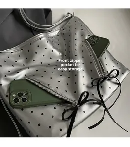 Detail of silver polka dot tote featuring dual front zipper pockets with ribbon bows