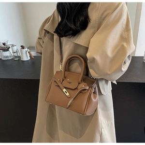 Brown lychee leather tote bag worn with trench coat, featuring metal lock and top handle