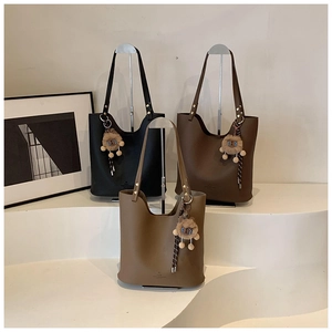 Close-up of three textured leather tote bags in black, dark brown, and tan with plush charms