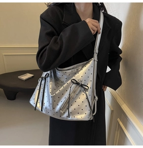 Close-up of silver tote bag with black polka dots and decorative bow detail on model