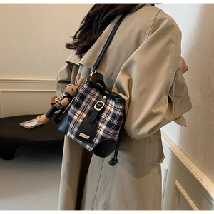 Klassieke geruite emmer tas met lederen bies en konijntje hanger op een beige trenchcoat