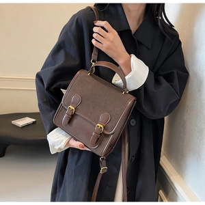 Detail of vintage dark brown leather crossbody bag with dual golden buckles and mix textures