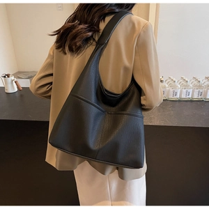 Macro side view of a large black leather hobo bag with textured grain and seamless strap