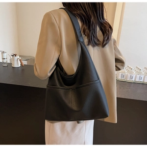 Detail view of a black pebbled leather tote bag worn by a model in a casual setting