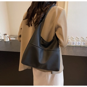 Detailed view of black hobo bag with pebble texture and large front pockets worn by model