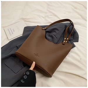 Detail of dark brown leather tote bag showing grainy texture and golden rivets
