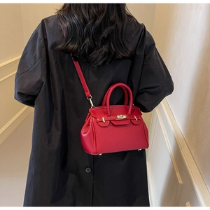 Detail of red leather crossbody bag with litchi texture and gold metal lock on black coat