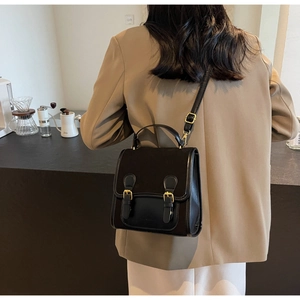Detail of a vintage black satchel bag with double gold buckles on a khaki suit