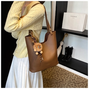 Macro detail of brown litchi pattern leather tote bag with a plush lion charm