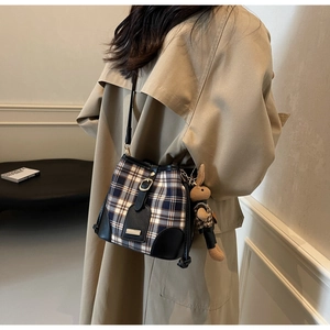 Detail van geblokte emmertas met een konijnenhanger gedragen op een beige trenchcoat