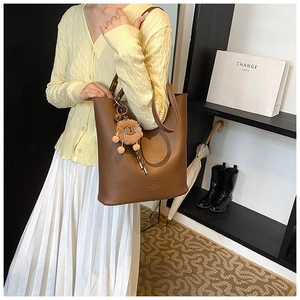 Brown lychee leather tote bag featuring a plush lion charm and embossed logo detail