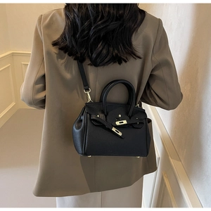 Detail view of mini black litchi leather handbag with gold hardware on a model jacket