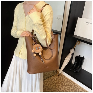 Brown lychee grain tote bag with plush lion charm shown worn over the shoulder