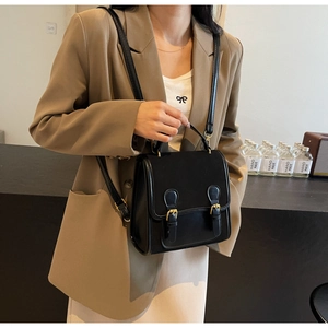 Detail shot of vintage black crossbody bag with double gold buckles on a model
