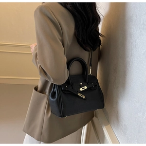 Detail of black lychee grain leather handbag with gold hardware and shoulder strap