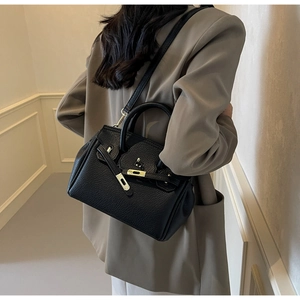 Detail of black lychee grain leather handbag with gold hardware and clasp closure
