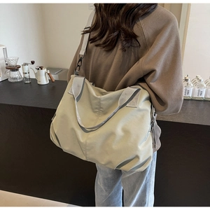 Detail of light grey-green nylon tote bag with wide strap in a minimalist cafe setting