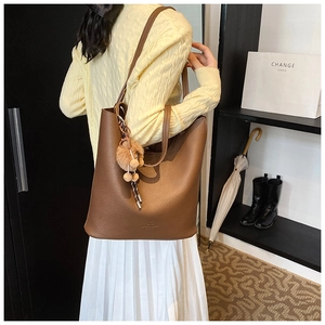 Brown lychee leather tote bag featuring a decorative pom-pom tassel charm on the side