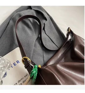 Détail d'un grand sac en cuir marron avec breloque smiley sur une veste grise