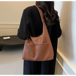 Brown leather tote bag featuring two front pockets and minimalist wide shoulder straps