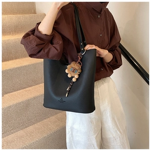 Detail of black pebbled leather bucket bag with a cute lion plush pendant accessory