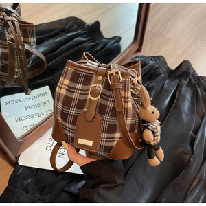 Detailopname van bruine ruitjes emmer tas met schattige konijnen hanger en leer.