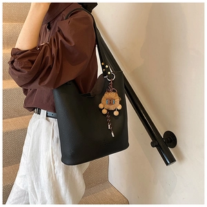 Detail of black bucket bag with lychee texture and cute lion charm on a female model