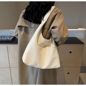 Model wearing a large cream faux leather tote bag with exterior pocket for daily commute