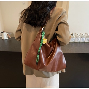 Grand sac à main marron en cuir souple avec pendentif smiley porté par un modèle