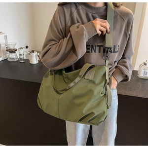Olive green nylon tote bag with wide shoulder strap shown in a casual lifestyle setting