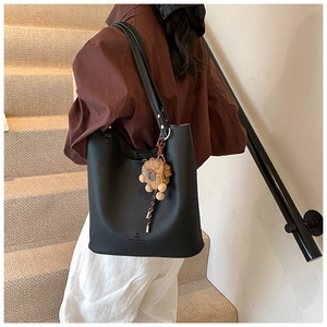 Detail of black pebbled leather bucket bag with a plush lion charm on model