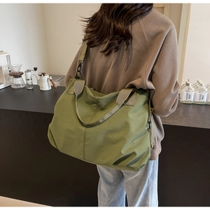 Olive green tote bag with adjustable strap shown from behind in a cozy cafe setting