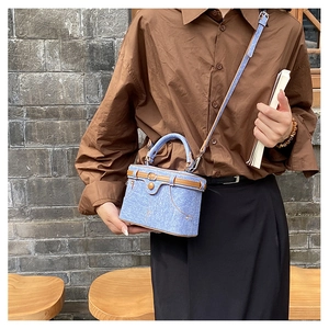 Detail of blue denim box bag featuring brown leather trim and metal clasp on a model