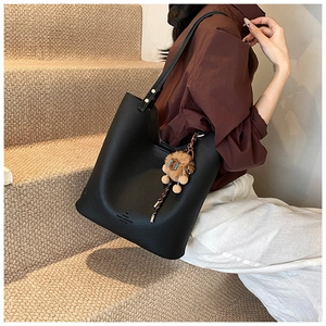 Close-up of black litchi grain leather bucket bag with cute lion plush charm