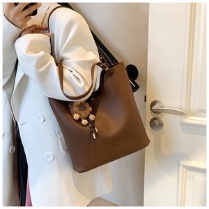 Detail of dark brown pebble leather tote bag with cute bear charm and golden logo