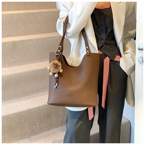 Close-up of brown litchi pattern leather tote bag with stylish lion plush pendant